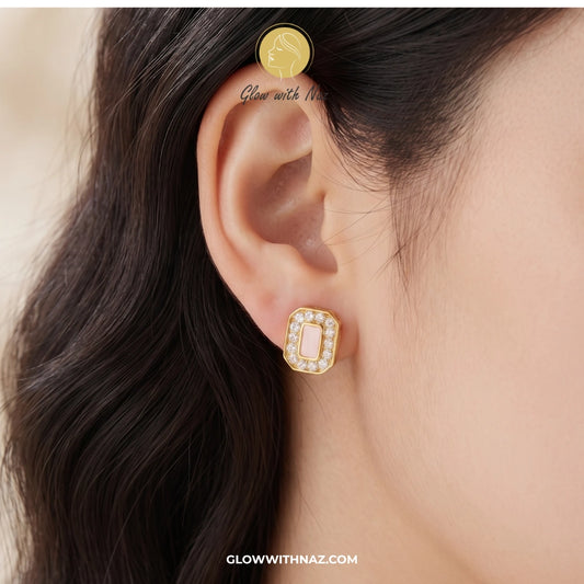 A close-up of a model's ear wearing a gold-toned rectangular stud earring with a central pale pink stone and small clear stones around it. The image includes the text 'Glow with NAZ' and 'GLOWWITHNAZ. studs earrings, small earrings, girls earrings, simple earrings, earrings for girls, black earrings, earrings, ear rings, earrings tops, stud earrings, tops earrings, aesthetic earrings, hoop earrings, drop earrings, diamond earrings, pink earrings, green earrings, ear ring, earrings for women, flower earrings