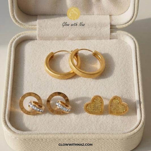 A set of gold-toned earrings displayed inside an open cream jewelry box. The set includes a pair of textured hoop earrings, a pair of ring-and-stud earrings with clear stones, and a pair of textured heart stud earrings. studs earrings, small earrings, girls earrings, simple earrings, earrings for girls, black earrings, earrings, ear rings, earrings tops, stud earrings, tops earrings, aesthetic earrings, hoop earrings, drop earrings, diamond earrings, pink earrings, green earrings, ear ring, earrings for wom