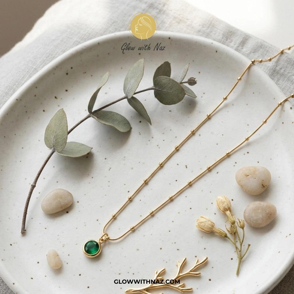Gold necklace with a green gemstone on a white plate with eucalyptus leaves and stones. necklace, pendant necklace, necklace set, locket set, simple necklace, pendant set, pendant, chain necklace, diamond pendant, diamond necklace, locket necklace, neck chain, girls locket, heart locket, pendant for girls, necklace for girls, heart necklace, locket for girls, diamond locket, pendant necklace for girls, heart chain locket, stainless steel necklace, double chain necklace, ruby necklace, neck chain for girls,