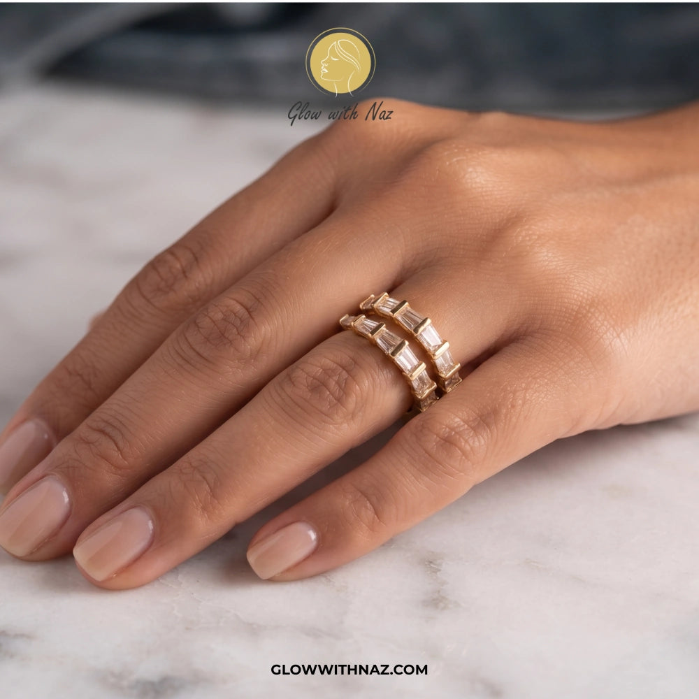 A close-up of a hand wearing two stacked gold rings with rectangular clear stones, resting on a light marble surface. A logo for Glow With Naz is visible at the top, and the website glowwithnaz. ring, girls rings, rings for girls, rings simple, simple rings, stainless steel jewelry, jewellery set, aesthetic jewelry, simple jewellery, chain, jewelry, artificial jewellery