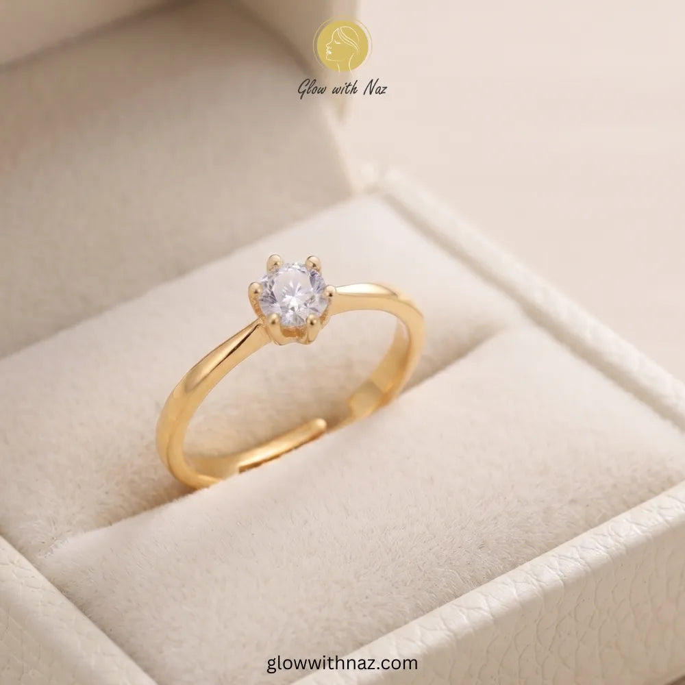 A gold ring with a single round clear gemstone in a prong setting, displayed inside a cream-colored jewelry box. The brand name 'Glow with Naz' is visible at the top, and a website URL is visible at the bottom. ring, girls rings, rings for girls, rings simple, simple rings, stainless steel jewelry, jewellery set, aesthetic jewelry, simple jewellery, chain, jewelry, artificial jewellery