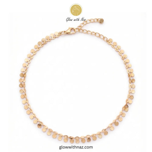 Flat lay of an unclasped gold anklet featuring small textured coin charms and an adjustable lobster clasp against a clean white background