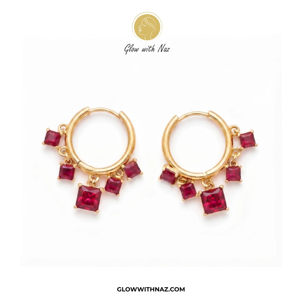 A pair of gold huggie hoop earrings with dangling square-cut red gemstones, displayed on a clean white background with the brand logo 'Glow with Naz' at the top. studs earrings, small earrings, girls earrings, simple earrings, earrings for girls, black earrings, earrings, ear rings, earrings tops, stud earrings, tops earrings, aesthetic earrings, hoop earrings, drop earrings, diamond earrings, pink earrings, green earrings, ear ring, earrings for women, flower earrings, golden earrings, bali earrings, ear j