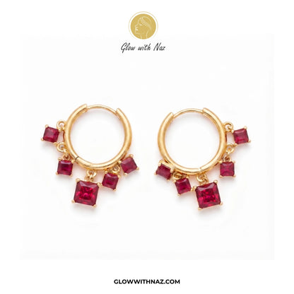 A pair of gold huggie hoop earrings with dangling square-cut red gemstones, displayed on a clean white background with the brand logo 'Glow with Naz' at the top. studs earrings, small earrings, girls earrings, simple earrings, earrings for girls, black earrings, earrings, ear rings, earrings tops, stud earrings, tops earrings, aesthetic earrings, hoop earrings, drop earrings, diamond earrings, pink earrings, green earrings, ear ring, earrings for women, flower earrings, golden earrings, bali earrings, ear j