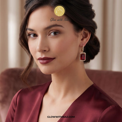 A close-up portrait of a woman wearing a dangling rectangular red gemstone earring with a gold-toned border. The image includes Glow with Naz branding and text overlays. studs earrings, small earrings, girls earrings, simple earrings, earrings for girls, black earrings, earrings, ear rings, earrings tops, stud earrings, tops earrings, aesthetic earrings, hoop earrings, drop earrings, diamond earrings, pink earrings, green earrings, ear ring, earrings for women, flower earrings, golden earrings, bali earring