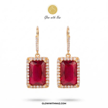 A pair of gold drop earrings featuring rectangular emerald-cut deep red gemstones surrounded by small clear stones, shown on a white background with Glow with Naz branding. studs earrings, small earrings, girls earrings, simple earrings, earrings for girls, black earrings, earrings, ear rings, earrings tops, stud earrings, tops earrings, aesthetic earrings, hoop earrings, drop earrings, diamond earrings, pink earrings, green earrings, ear ring, earrings for women, flower earrings, golden earrings, bali earr