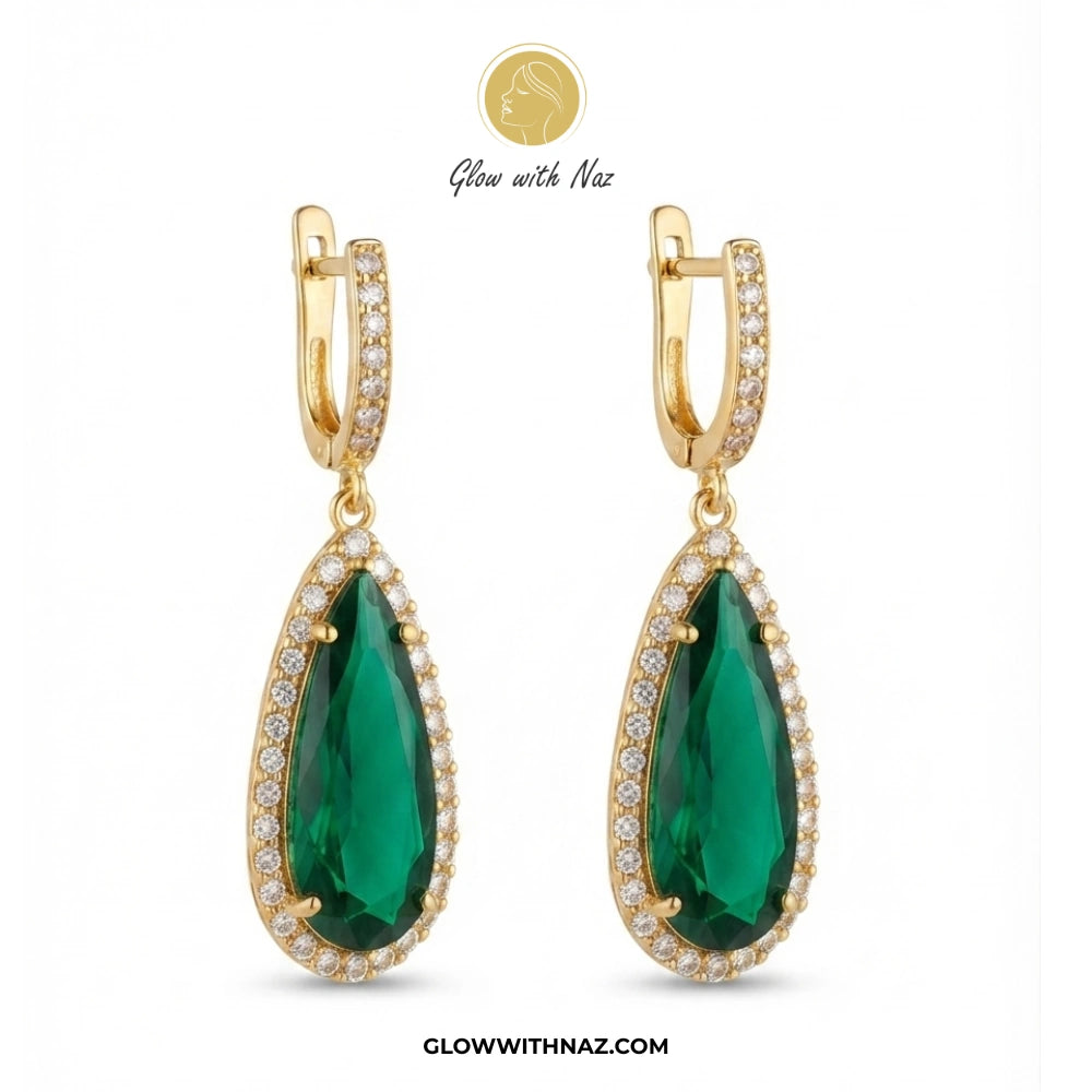 A pair of gold huggie drop earrings featuring large teardrop-shaped emerald green stones surrounded by small clear pavé stones, shown on a white background with the brand name Glow with Naz. studs earrings, small earrings, girls earrings, simple earrings, earrings for girls, black earrings, earrings, ear rings, earrings tops, stud earrings, tops earrings, aesthetic earrings, hoop earrings, drop earrings, diamond earrings, pink earrings, green earrings, ear ring, earrings for women, flower earrings, golden e