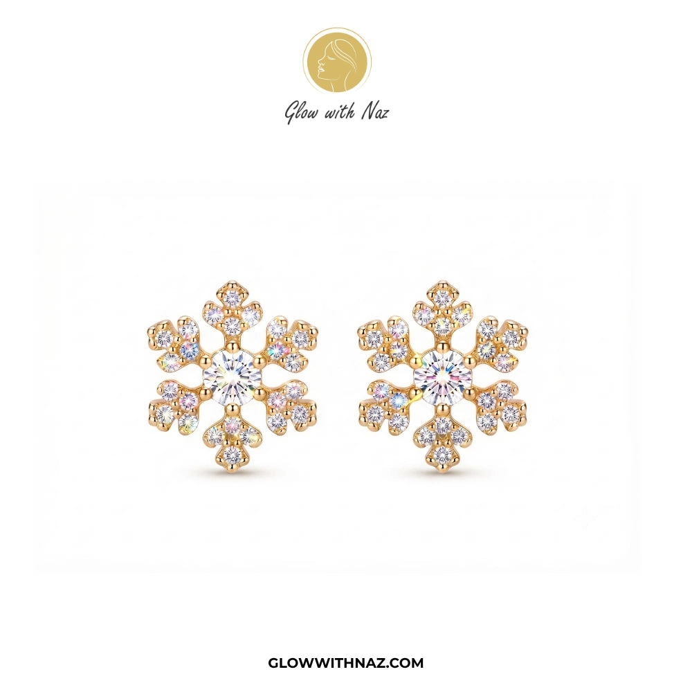 A pair of gold snowflake-shaped stud earrings adorned with clear gemstones, displayed on a clean white background with the brand logo 'Glow with Naz' at the top and 'GLOWWITHNAZ.COM' at the bottom. studs earrings, small earrings, girls earrings, simple earrings, earrings for girls, black earrings, earrings, ear rings, earrings tops, stud earrings, tops earrings, aesthetic earrings, hoop earrings, drop earrings, diamond earrings, pink earrings, green earrings, ear ring, earrings for women, flower earrings, g