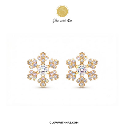 A pair of gold snowflake-shaped stud earrings adorned with clear gemstones, displayed on a clean white background with the brand logo 'Glow with Naz' at the top and 'GLOWWITHNAZ.COM' at the bottom. studs earrings, small earrings, girls earrings, simple earrings, earrings for girls, black earrings, earrings, ear rings, earrings tops, stud earrings, tops earrings, aesthetic earrings, hoop earrings, drop earrings, diamond earrings, pink earrings, green earrings, ear ring, earrings for women, flower earrings, g