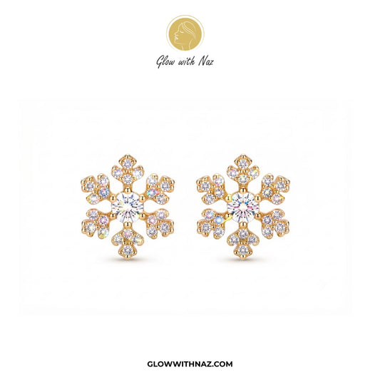 A pair of gold snowflake-shaped stud earrings adorned with clear gemstones, displayed on a clean white background with the brand logo 'Glow with Naz' at the top and 'GLOWWITHNAZ.COM' at the bottom. studs earrings, small earrings, girls earrings, simple earrings, earrings for girls, black earrings, earrings, ear rings, earrings tops, stud earrings, tops earrings, aesthetic earrings, hoop earrings, drop earrings, diamond earrings, pink earrings, green earrings, ear ring, earrings for women, flower earrings, g