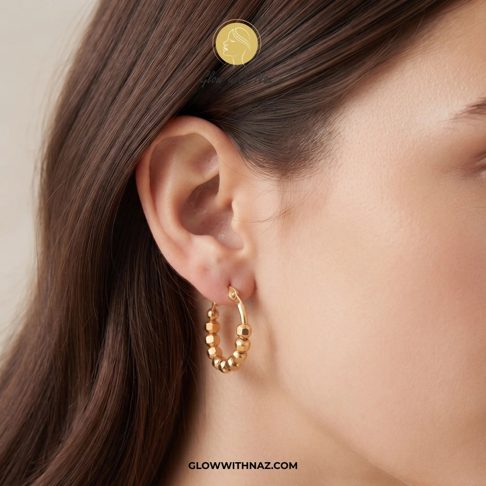 A close-up of a model's ear wearing a small gold hoop earring with beaded detailing. A coin is placed near the top of the head to show the earring's scale. studs earrings, small earrings, girls earrings, simple earrings, earrings for girls, black earrings, earrings, ear rings, earrings tops, stud earrings, tops earrings, aesthetic earrings, hoop earrings, drop earrings, diamond earrings, pink earrings, green earrings, ear ring, earrings for women, flower earrings, golden earrings, bali earrings, ear jewelle