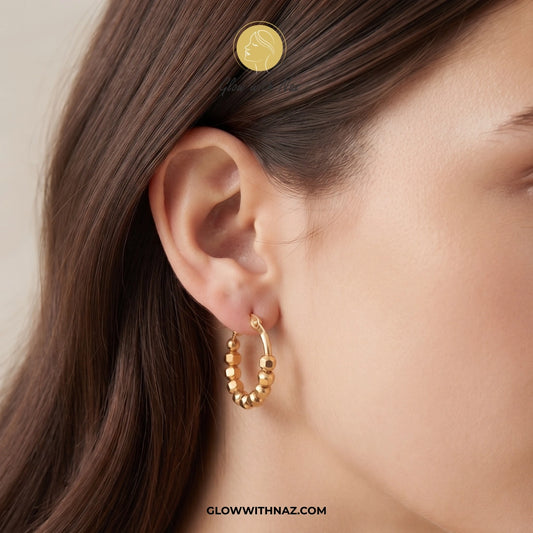 A close-up of a model's ear wearing a small gold hoop earring with beaded detailing. A coin is placed near the top of the head to show the earring's scale. studs earrings, small earrings, girls earrings, simple earrings, earrings for girls, black earrings, earrings, ear rings, earrings tops, stud earrings, tops earrings, aesthetic earrings, hoop earrings, drop earrings, diamond earrings, pink earrings, green earrings, ear ring, earrings for women, flower earrings, golden earrings, bali earrings, ear jewelle