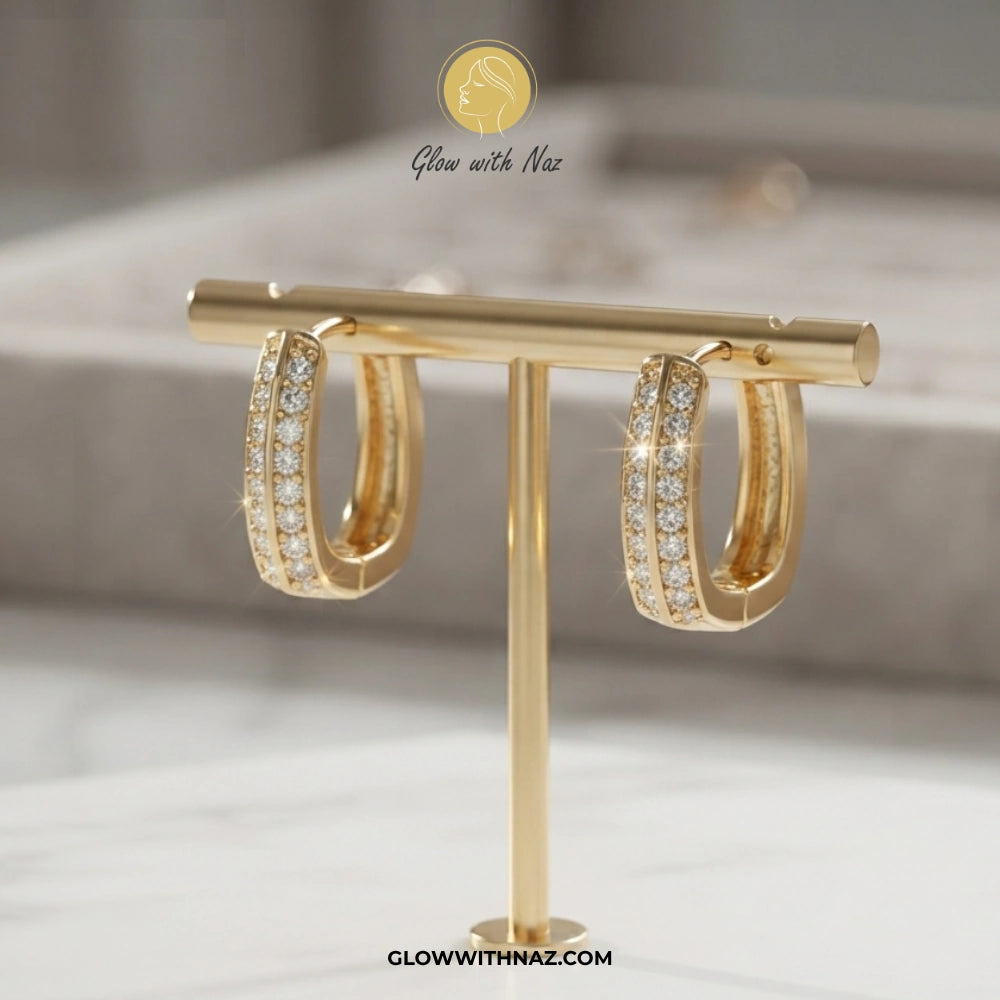 A pair of gold hoop earrings with pavé-set clear stones, displayed on a gold T-stand. The brand logo 'Glow with Naz' is visible at the top and 'GLOWWITHNAZ. studs earrings, small earrings, girls earrings, simple earrings, earrings for girls, black earrings, earrings, ear rings, earrings tops, stud earrings, tops earrings, aesthetic earrings, hoop earrings, drop earrings, diamond earrings, pink earrings, green earrings, ear ring, earrings for women, flower earrings, golden earrings, bali earrings, ear jewell