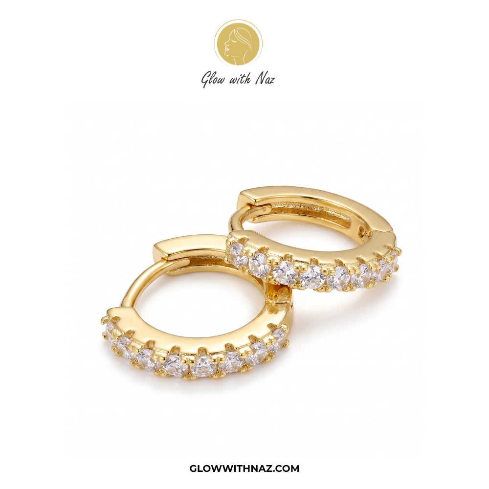 A pair of gold huggie hoop earrings adorned with clear pavé-set cubic zirconia stones, displayed on a clean white background with a brand logo 'Glow with Naz' at the top and website URL at the bottom. studs earrings, small earrings, girls earrings, simple earrings, earrings for girls, black earrings, earrings, ear rings, earrings tops, stud earrings, tops earrings, aesthetic earrings, hoop earrings, drop earrings, diamond earrings, pink earrings, green earrings, ear ring, earrings for women, flower earrings