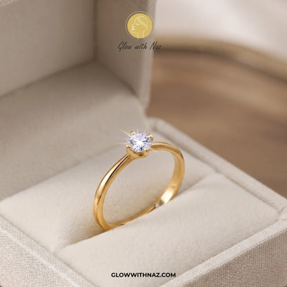 A gold solitaire ring with a clear round gemstone displayed inside an open beige jewelry box. The brand name 'Glow with Naz' is visible as a watermark at the top and in the URL at the bottom. ring, girls rings, rings for girls, rings simple, simple rings, stainless steel jewelry, jewellery set, aesthetic jewelry, simple jewellery, chain, jewelry, artificial jewellery