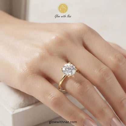 A close-up of a hand wearing a yellow gold solitaire ring with a clear round-cut gemstone. The brand logo 'Glow with Naz' is visible at the top of the image. ring, girls rings, rings for girls, rings simple, simple rings, stainless steel jewelry, jewellery set, aesthetic jewelry, simple jewellery, chain, jewelry, artificial jewellery