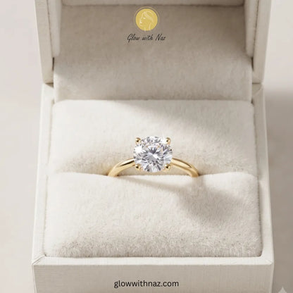 A yellow gold solitaire engagement ring with a round-cut clear gemstone, presented in a white jewelry box with a soft cream insert. The brand name 'Glow with Naz' is visible on the inside lid and as a watermark at the bottom. ring, girls rings, rings for girls, rings simple, simple rings, stainless steel jewelry, jewellery set, aesthetic jewelry, simple jewellery, chain, jewelry, artificial jewellery