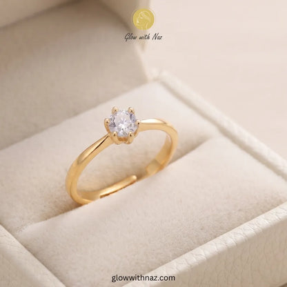 A gold ring with a single round clear gemstone in a prong setting, displayed inside a cream-colored jewelry box. The brand name 'Glow with Naz' is visible at the top, and a website URL is visible at the bottom. ring, girls rings, rings for girls, rings simple, simple rings, stainless steel jewelry, jewellery set, aesthetic jewelry, simple jewellery, chain, jewelry, artificial jewellery