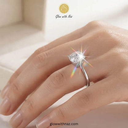 A silver solitaire ring with a heart-shaped clear gemstone worn on a hand, featuring a bright starburst effect and a gold-toned logo for Glow with Naz at the top. ring, girls rings, rings for girls, rings simple, simple rings, stainless steel jewelry, jewellery set, aesthetic jewelry, simple jewellery, chain, jewelry, artificial jewellery