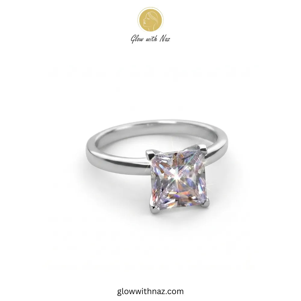 A silver band ring featuring a princess-cut clear gemstone in a four-prong setting, shown on a plain white background with a 'Glow with Naz' logo at the top. ring, girls rings, rings for girls, rings simple, simple rings, stainless steel jewelry, jewellery set, aesthetic jewelry, simple jewellery, chain, jewelry, artificial jewellery