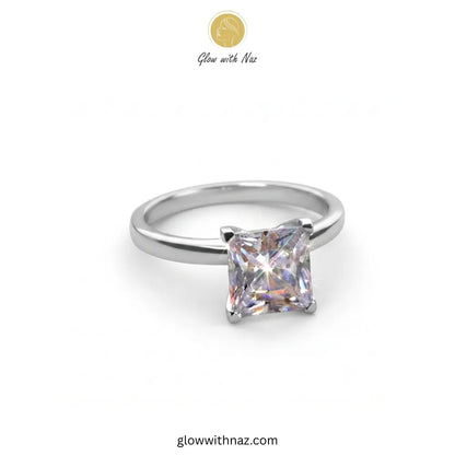A silver band ring featuring a princess-cut clear gemstone in a four-prong setting, shown on a plain white background with a 'Glow with Naz' logo at the top. ring, girls rings, rings for girls, rings simple, simple rings, stainless steel jewelry, jewellery set, aesthetic jewelry, simple jewellery, chain, jewelry, artificial jewellery