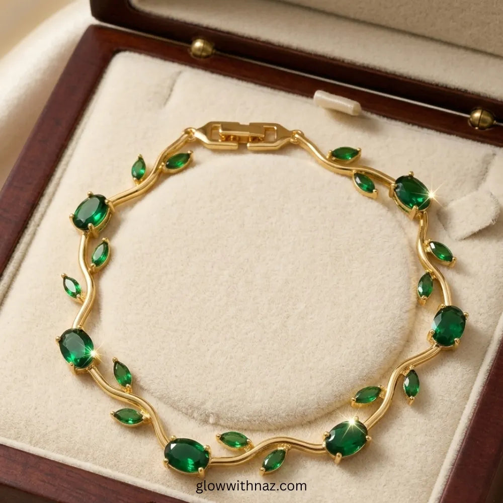 A gold chain bracelet decorated with multiple green emerald-cut gemstones, displayed inside an open dark wood jewelry box with a cream velvet lining. Tulip Rapunzel bracelet, floral tulip bracelet, Rapunzel inspired jewelry, aesthetic tulip bracelet, trendy charm bracelet, stainless steel tulip bracelet, gold plated flower bracelet, delicate floral wrist accessory, cute aesthetic jewelry, viral tulip bracelet, Rapunzel theme accessories, dainty floral bracelet, crystal tulip charm, stacking bracelets for wo