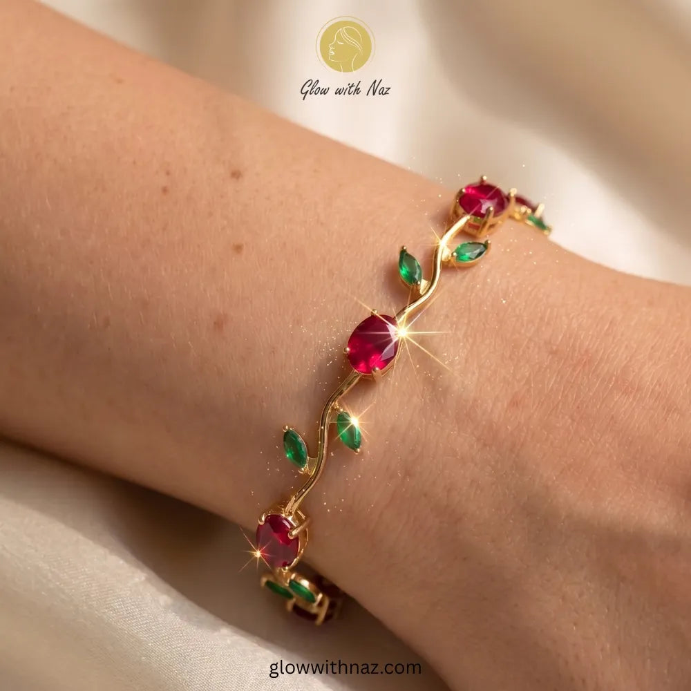 Gold bracelet with red and green gemstones on a wrist, brand 'Glow with Naz' visible. Tulip Rapunzel bracelet, floral tulip bracelet, Rapunzel inspired jewelry, aesthetic tulip bracelet, trendy charm bracelet, stainless steel tulip bracelet, gold plated flower bracelet, delicate floral wrist accessory, cute aesthetic jewelry, viral tulip bracelet, Rapunzel theme accessories, dainty floral bracelet, crystal tulip charm, stacking bracelets for women, minimalist floral jewelry, spring aesthetic bracelet, elega