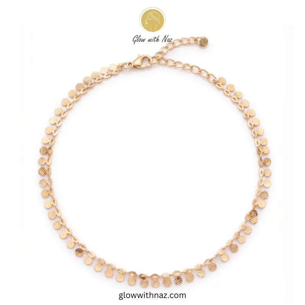 Flat lay of an unclasped gold anklet featuring small textured coin charms and an adjustable lobster clasp against a clean white background